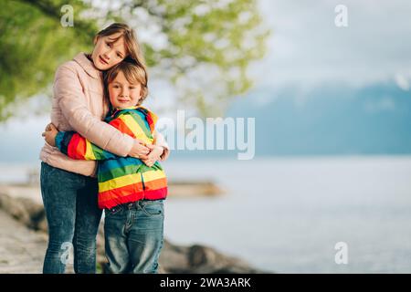 Two little kids playing together by lake Geneva on a cold day, hugging each other, wearing warm jackets Stock Photo