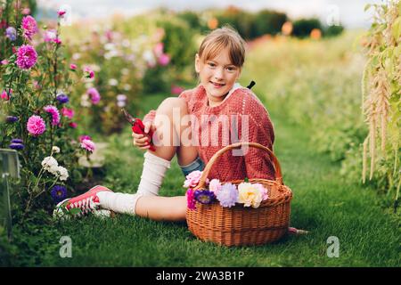 Pretty little girl working in autumn garden, child taking care of colorful chrysanthemum, gardener teenager enjoying warm and sunny day Stock Photo