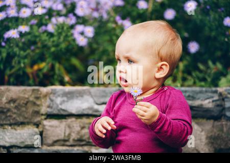 Outdoor portrait of adorable 9-12 month old baby girl playing with purple flowers Stock Photo