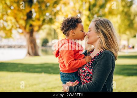 Happy young mother holding sweet toddler boy, family having fun together outside on a nice sunny day Stock Photo