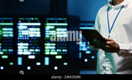 IT specialist walking through server rows performing data backups, close up. Serviceman using tablet to make sure electric generators are able to ensure operational continuity Stock Photo
