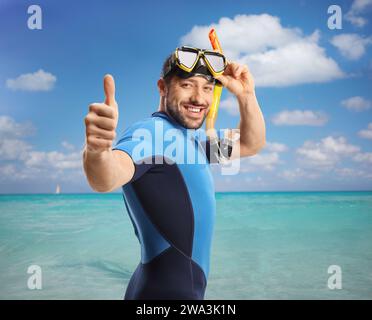 Young man in the sea wearing a diving suit and mask and gesturing thumbs up Stock Photo