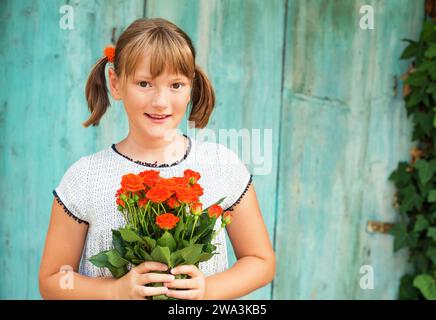 Outdoor portrait of a yong little girl of 9 years old, wearing white dress, holding fresh bouquet of beautiful orange roses Stock Photo