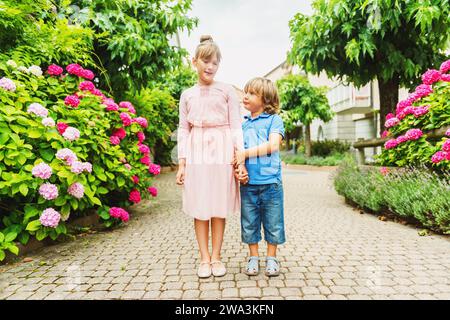 Two kids wearing fashion shoes, little boy wearing denim shorts and blue leather sandals, schoolgirl in pink dress and ballerina shoes Stock Photo
