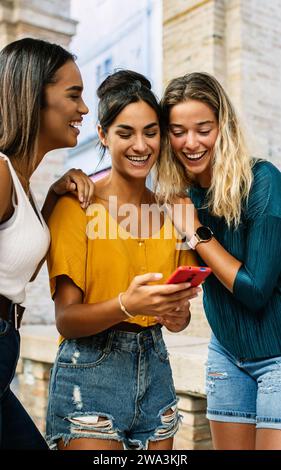 Multiracial young female friends laughing while using mobile phone outdoors. Stock Photo