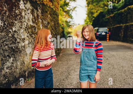 Outdoor portrait of two funny preteen girls wearing denim jeans, stripe roll neck pullovers, fashion for teens Stock Photo