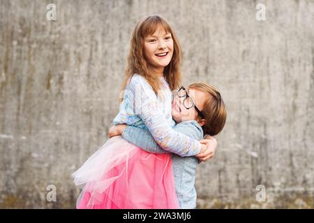 Outdoor portrait of two funny fashion kids, holding drinks, wearing blue and pink clothes Stock Photo