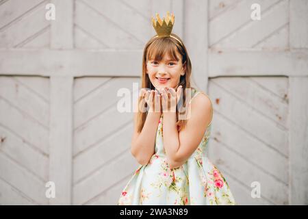 Young little 9-10 year old girl, wearing beautiful dress and gold crown headband, blowing a kiss Stock Photo