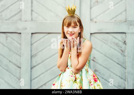 young little 9-10 year old girl, wearing beautiful dress and gold crown headband, sending a kiss Stock Photo