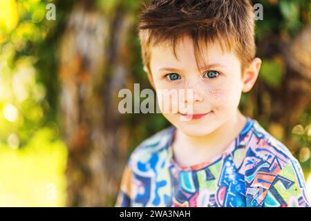 Outdoor close up portrait of adorable 5-6 year old red-haired boy with freckles on his face Stock Photo