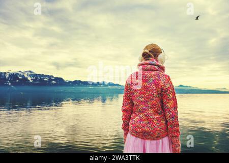 Adorable little girl admiring lake Geneva on a cold winter day, wearing warm pink pullover and earmuffs, back view Stock Photo