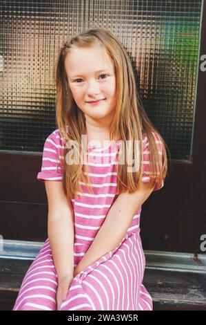 Outdoor portrait of adorable 6 year old girl wearing pink stripe dress Stock Photo