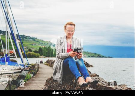 Middle age woman resting by the lake, using tablet pc outdoors Stock Photo