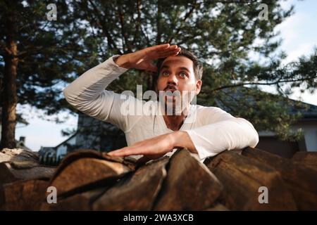 Concept of private life. Curious man spying on neighbours over firewood outdoors, low angle view Stock Photo