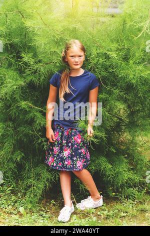 Kid girl playing in summer park, wearing blue t-shirt, denim skirt and white shoes Stock Photo