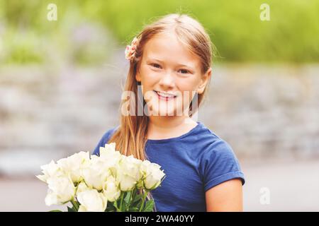 Outdoor portrait of a yong little girl of 9 years old, wearing blue tee shirt, holding fresh bouquet of beautiful white roses Stock Photo