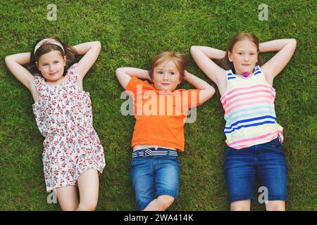 Happy children having fun outdoors. Kids playing in summer park. Little boy and two girls laying on green fresh grass Stock Photo