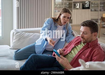 Worried woman suspects husband of cheating asks to see messages on phone. Mistrust in relationships. Stock Photo