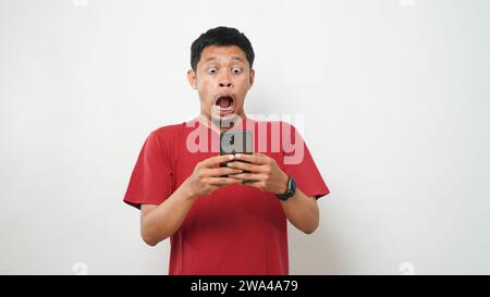 Wow face of Asian man shocked what he see in the smartphone on isolated grey background. Stock Photo