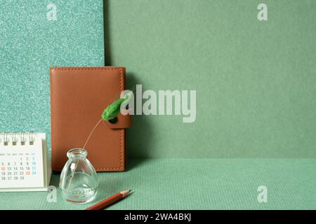 Diary notebook, calendar, vase of plant, colored pencil on desk. green wall background. planning office supply Stock Photo