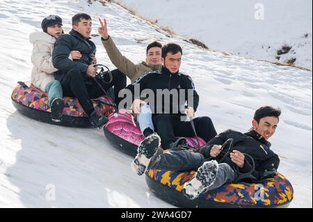 TAU SAMALY, KAZAKHSTAN - DECEMBER 23, 2023: happy Kazakhs friends tubing down a slide in winter with snow at the Tau Samaly recreation center in Kazakhstan Stock Photo