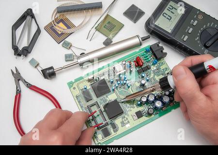 Close-up of a technician's hands in a workshop. The repairer is soldering an IC in a PLCC package to the circuit board of an electronic device. Stock Photo