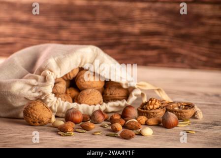 Almond nuts, hazelnuts, walnuts and sweet seeds in a burlap bag on a wooden background. Stock Photo