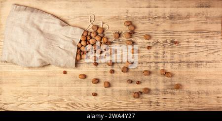 Large bag of burlap with walnuts and hazelnuts. Nuts are scattered on a large wooden board. Wooden background. Top view. Stock Photo