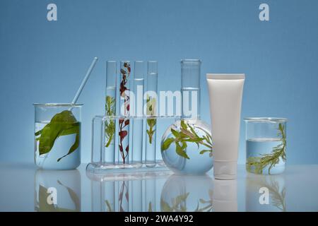 An empty white plastic tube decorated with laboratory equipment and fresh seaweed leaves on a backlit blue background .Mockup packaging, cosmetics des Stock Photo