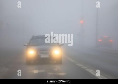 Front view of a black car with bright headlights driving on city street in dense fog. Stock Photo