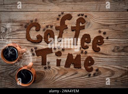 Coffee time written by ground coffee on textured wooden background. Two cups with hot coffee with steam. Stock Photo