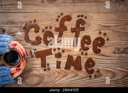 Coffee time written by ground coffee on a wooden background. Girl holding a cup of coffee with steam. Stock Photo