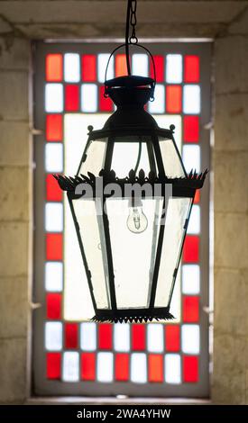ceiling lamp in iron, in front of the window with glass and stained glass of red squares. Stock Photo