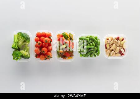 Frozen vegetables in plastic containers on white background. Frozen broccoli, green beans, cherry tomatoes, beans and bell pepper. Stock Photo