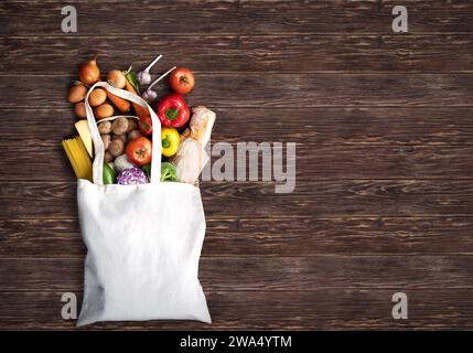 Eco friendly shopping fabric bag filled with fresh colorful vegetables on brown wooden background. Captured from above (top view, flat lay). Stock Photo
