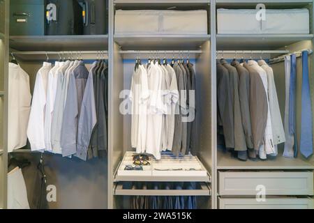 Explore the epitome of sophistication with a collection of meticulously hung men's suits and shirts in a well-organized closet. This scene exudes a re Stock Photo