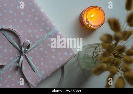 Wrapped holiday gift with burning candle and flowers in vase Stock Photo