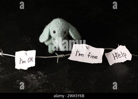 Paper pieces with barbed wire and toy elephant on dark background. Domestic violence concept Stock Photo