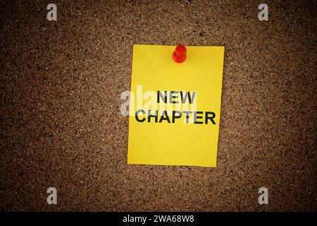A yellow paper note with the words New chapter on it pinned to a cork board. Close up. Stock Photo