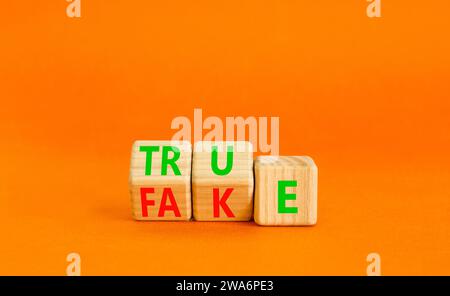Fake or true symbol. Turned wooden cubes and changed the word fake to true or vice versa. Beautiful orange table, orange background, copy space. Busin Stock Photo