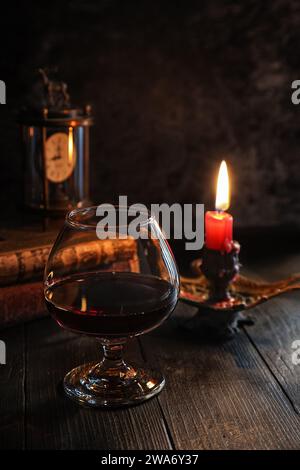 Vintage still life with old books, cloc, candle and a glass of red wine on rustic dark wooden board. Stock Photo