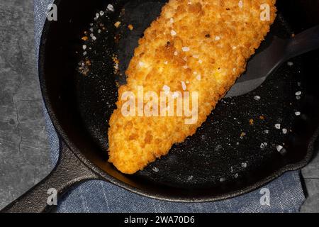 Pan fried breaded haddock fish in a cast iron frying pan. On a dark stone background Stock Photo