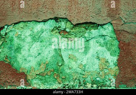 Peeled red plaster from a green wall. Abstract background from an abandoned damaged wall. Cracked plaster on the wall. Stock Photo