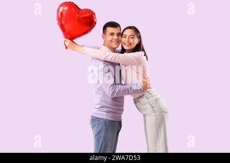 Young couple with heart-shaped balloon hugging on lilac background. Valentine's Day celebration Stock Photo