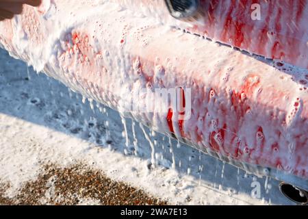 Soapy foam running off a red car at a car wash Stock Photo