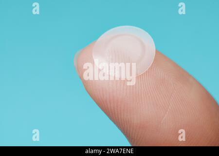 Close-up round acne patch on finger on blue background. Acne patches for treatment of pimple and rosacea close-up. Facial rejuvenation cleansing cosme Stock Photo