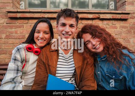 Group of three real classmates sitting at university campus. Group of young high school students looking at camera. Teenage multiracial people staring front. Adolescent schoolboys at academy break. High quality photo Stock Photo