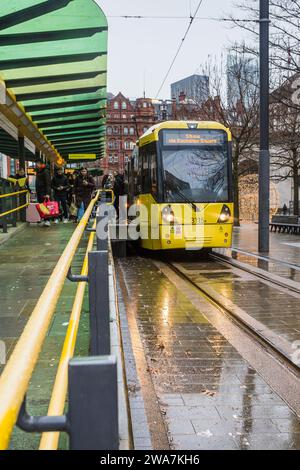 Passengers leave a yellow tram in the rain at St Peters Square station on the Manchester Metrolink transport network on 2 January 2024. Stock Photo