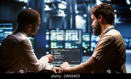 IT developers team writing server script code in data center on laptop terminal. Teamworking programmers doing maintenance work in high tech facility updating rigs software Stock Photo