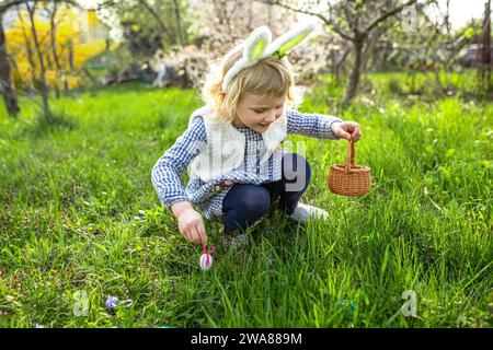 Gilr with painting eggs. Cute little child girl is wearing bunny ears. Easter hunt concept Stock Photo